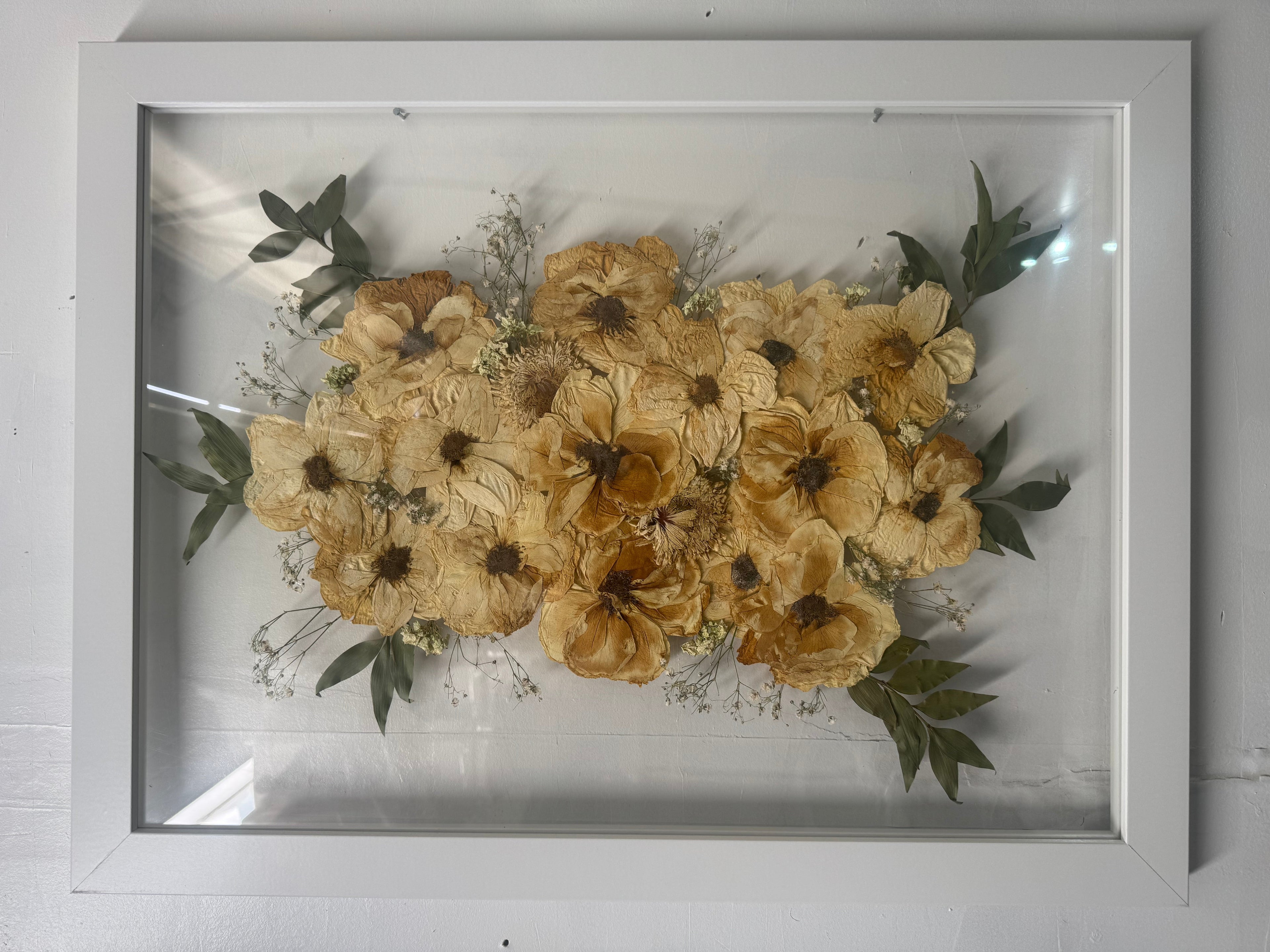 Framed artwork of pressed flowers on a white wall